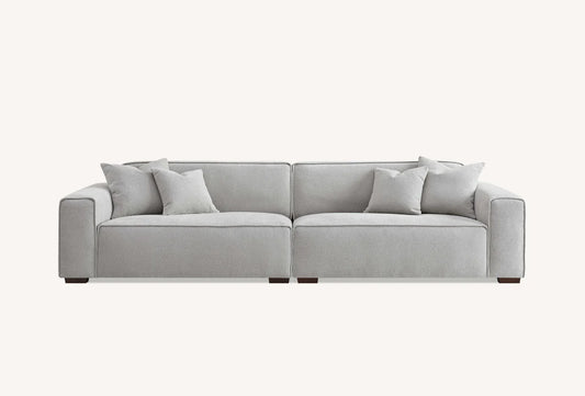 Large light grey sofa with plain white background with 4 cushions. 