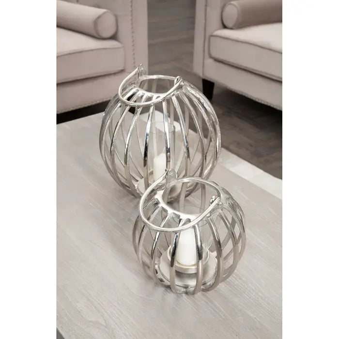 Our Aria Lantern, finished in silver, features an open frame structure with a cylindrical glass cover that will radiate a subtle glow around the room creating a soft, peaceful ambience whilst being a stylish accessory at all times of the day. A heavy duty, high quality silver product available in 2 sizes.