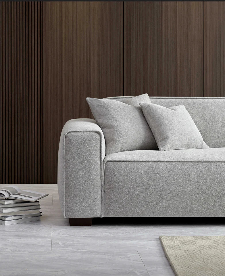 Close up of one side of light grey sofa, wood background and maagazines on the floor. 