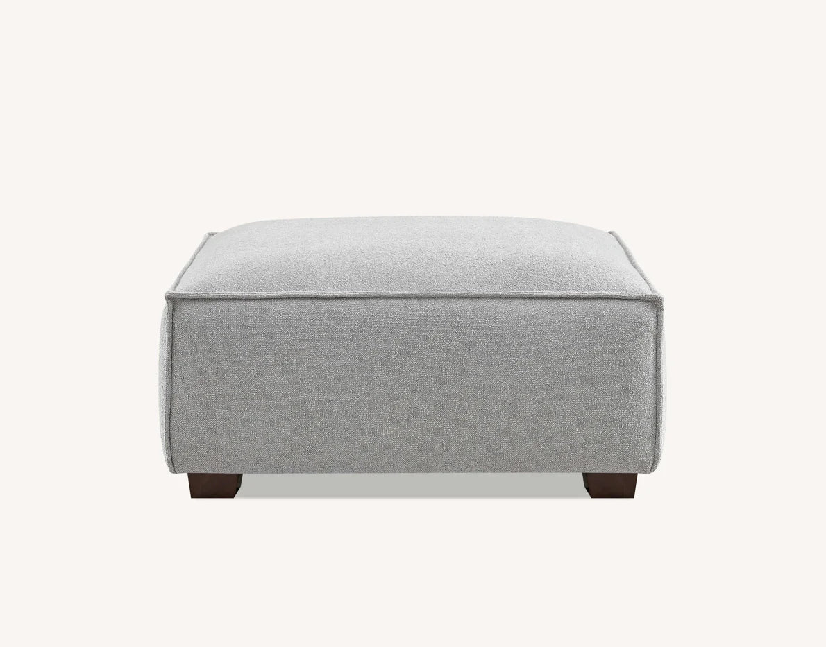 Pebble coloured footstool with  plain white background. 
