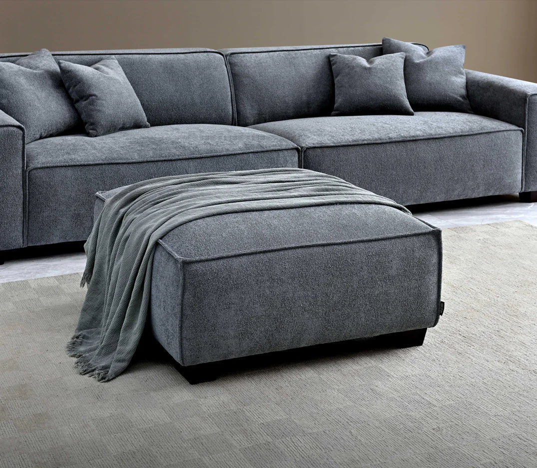 Close up of soft touch grey sofa with footstall in the foreground draped with a grey blanket. 