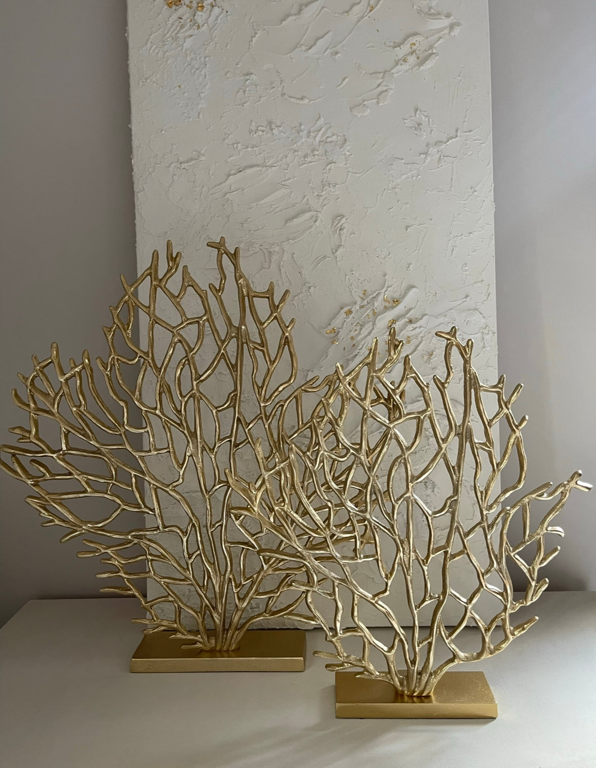 Gold ornament stands on a slim rectangular stand, and the sculpture spreads its branches upwards and outwards. 2 pictured with plain background. 

